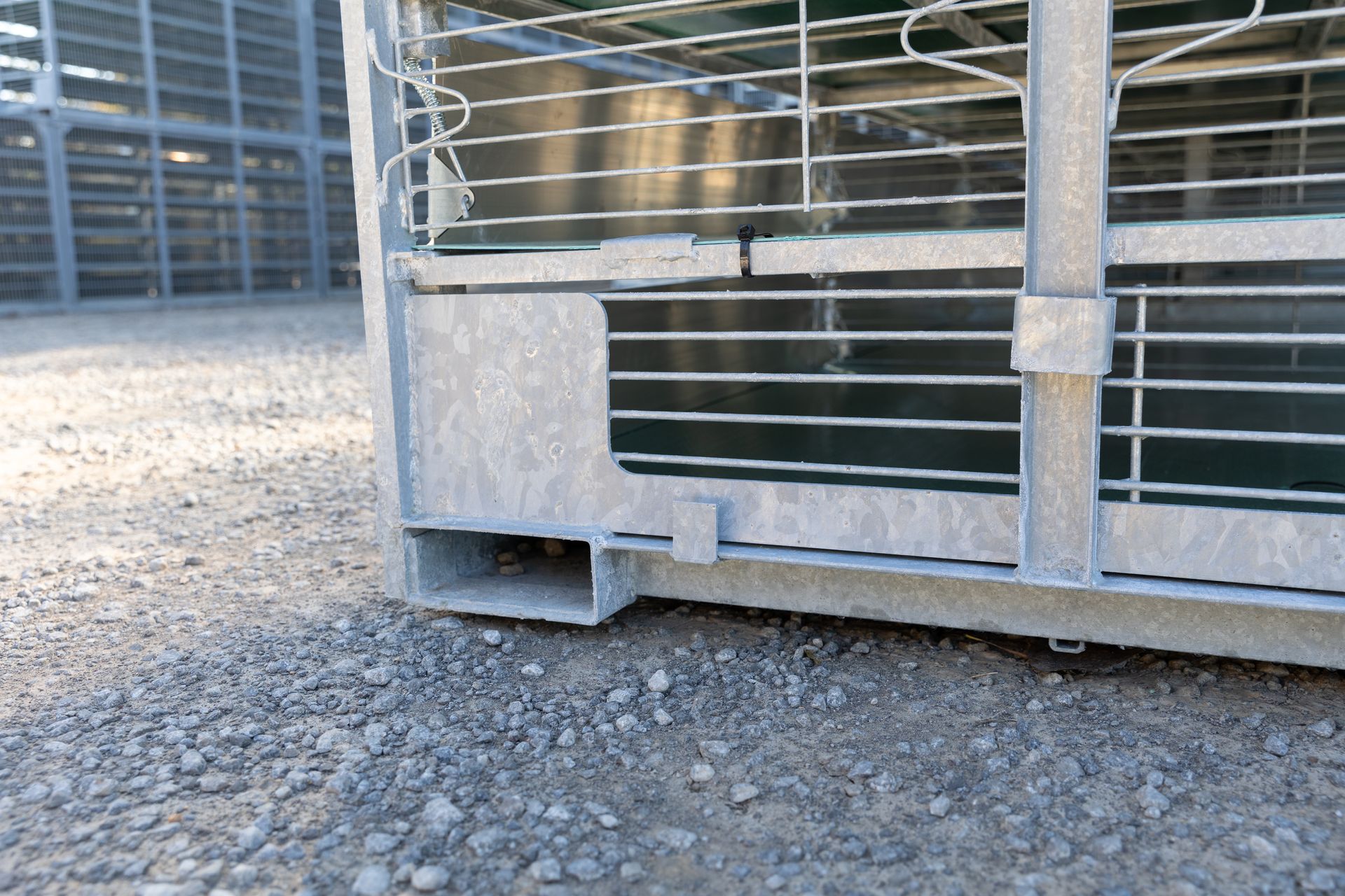 Close-up of a galvanized steel cage base with a forklift entry point on a gravel surface.