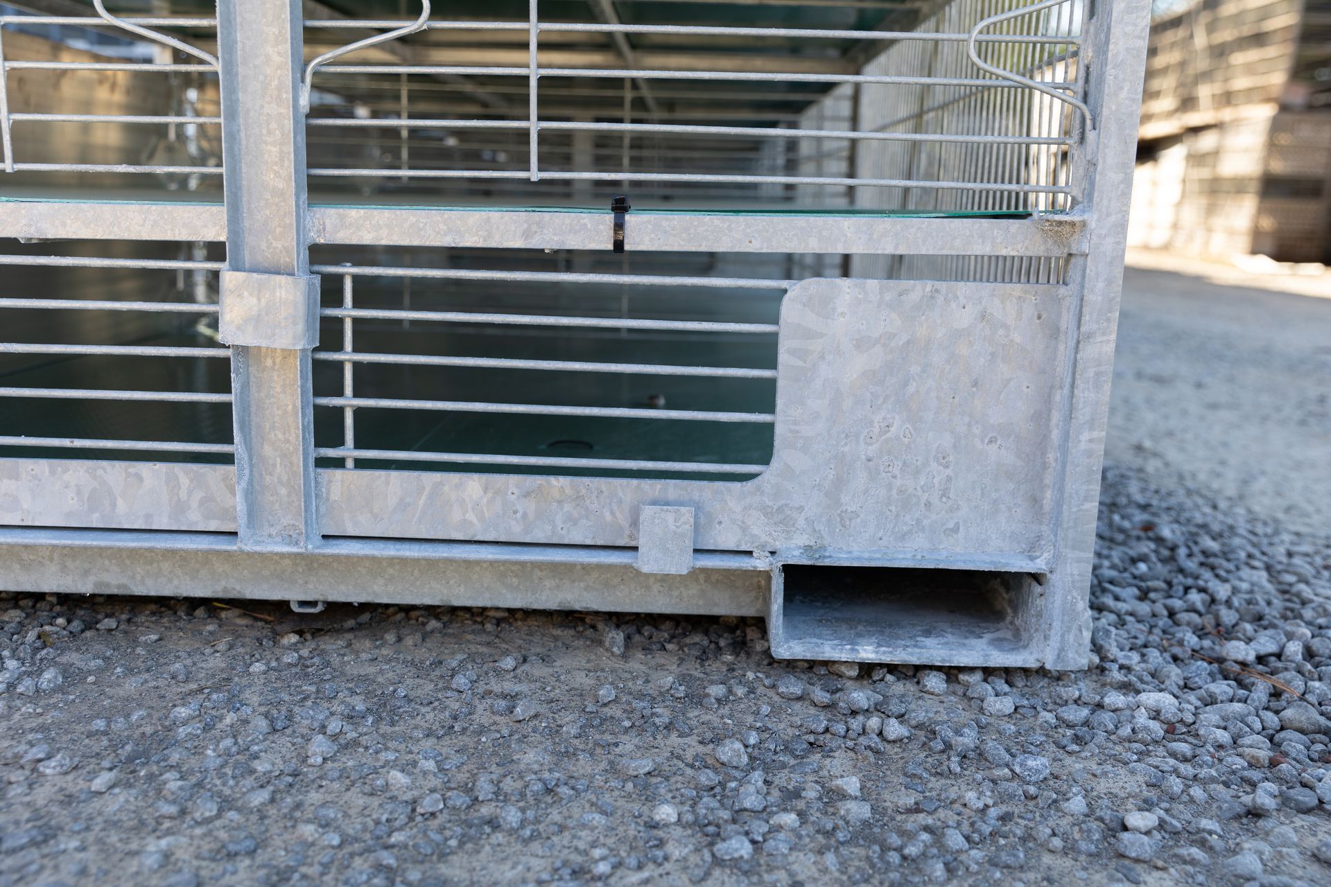 Close-up of a galvanized steel cage base with a forklift entry point on a gravel surface.