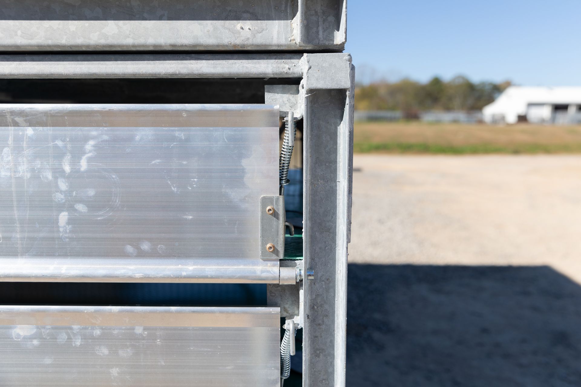 Metal panels stacked outdoors, on gravel, with a field and trees in the background.