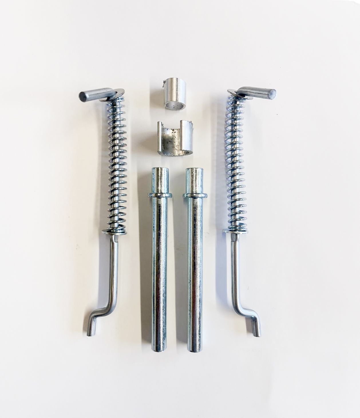 Metal hardware components, including two spring-loaded rods, two solid rods, and two cylindrical bushings, arranged on white.