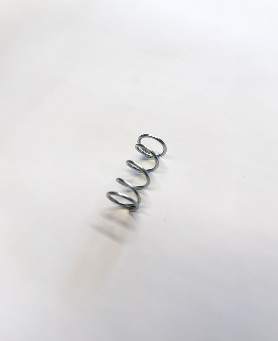 Small, silver metal coil spring on a white surface.