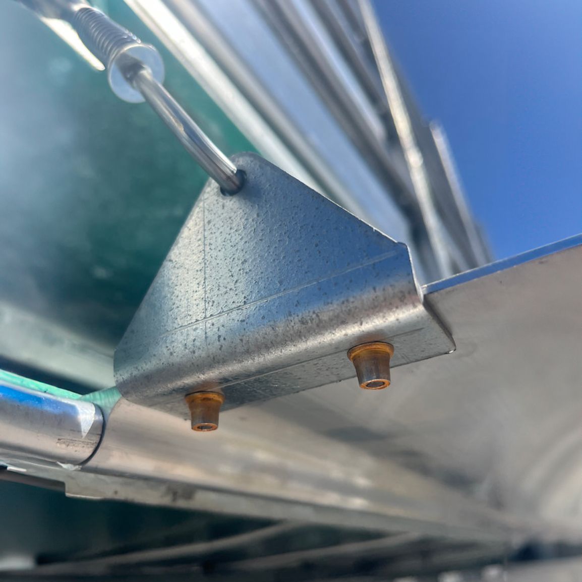 Close-up of a metal bracket attached to a green and silver structure with a wire and visible bolts.