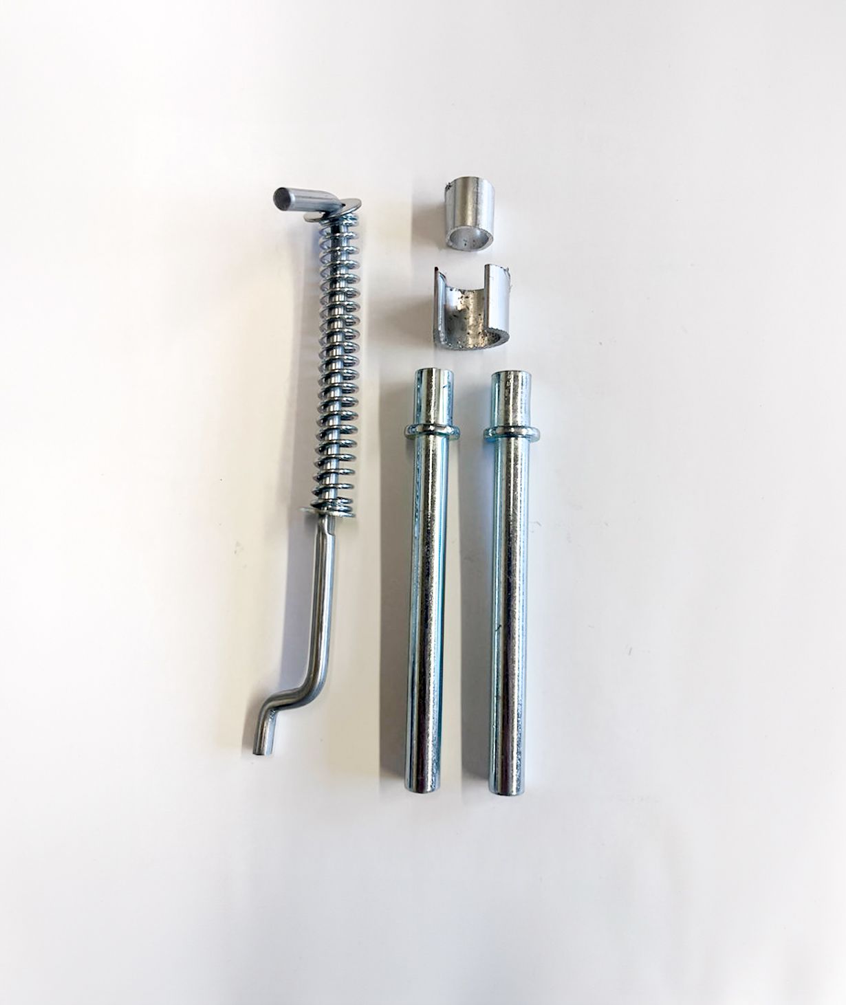 Silver brake caliper hardware set on a white surface, including a spring, pins, and clips.