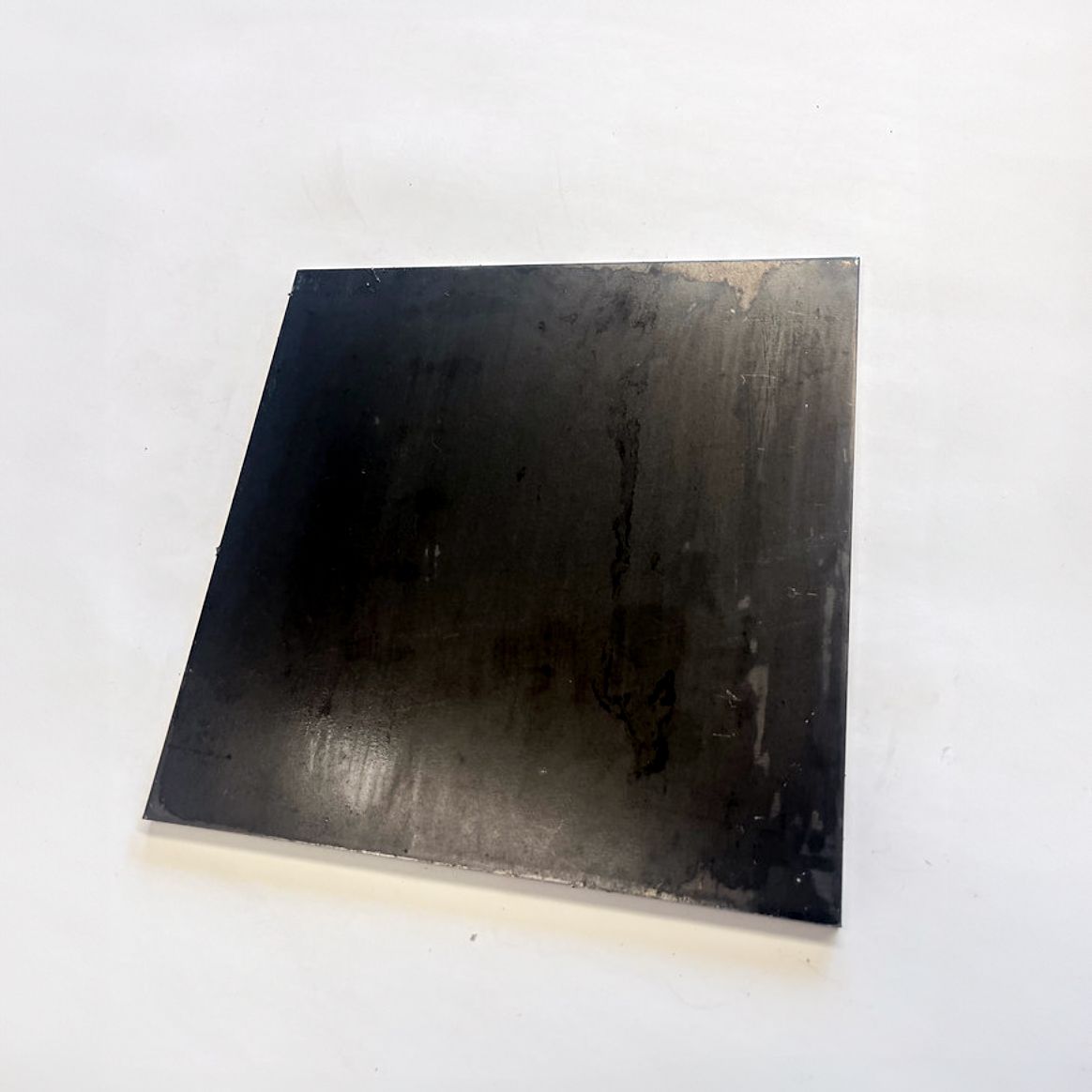 Dark, square metal plate against a white background.