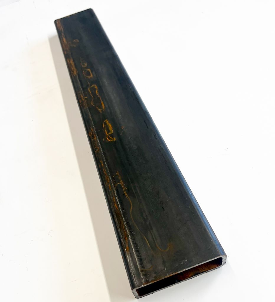 Rectangular steel tube with a dark, textured surface, lying on a white surface.