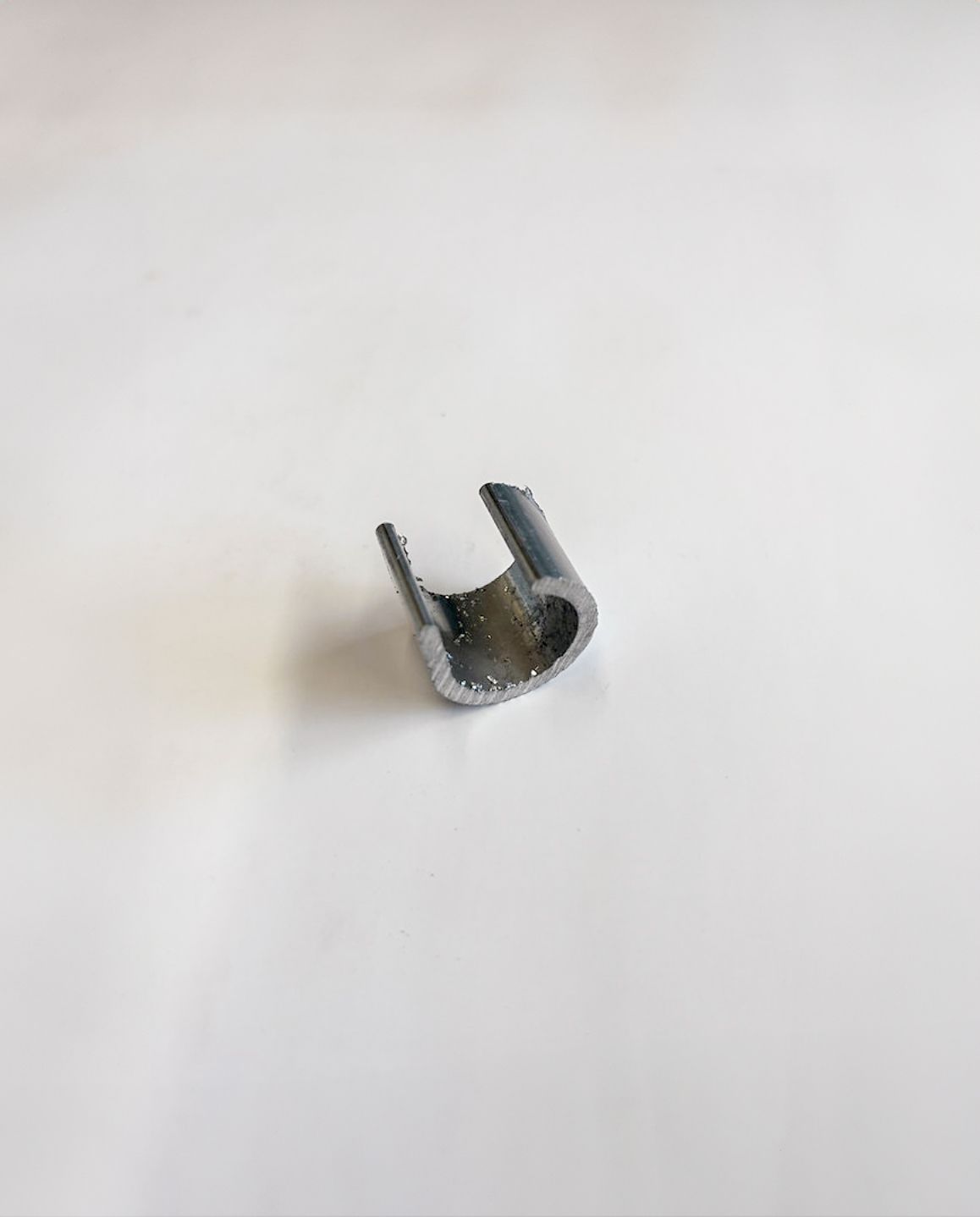 A small, gray metal bracket, U-shaped, sits against a white background.