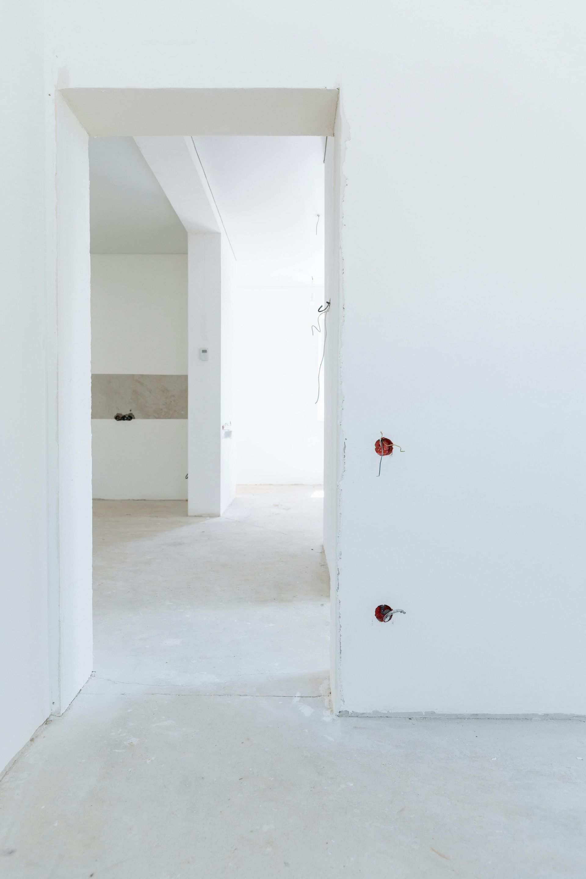 An empty room with white walls and a doorway leading to a kitchen.