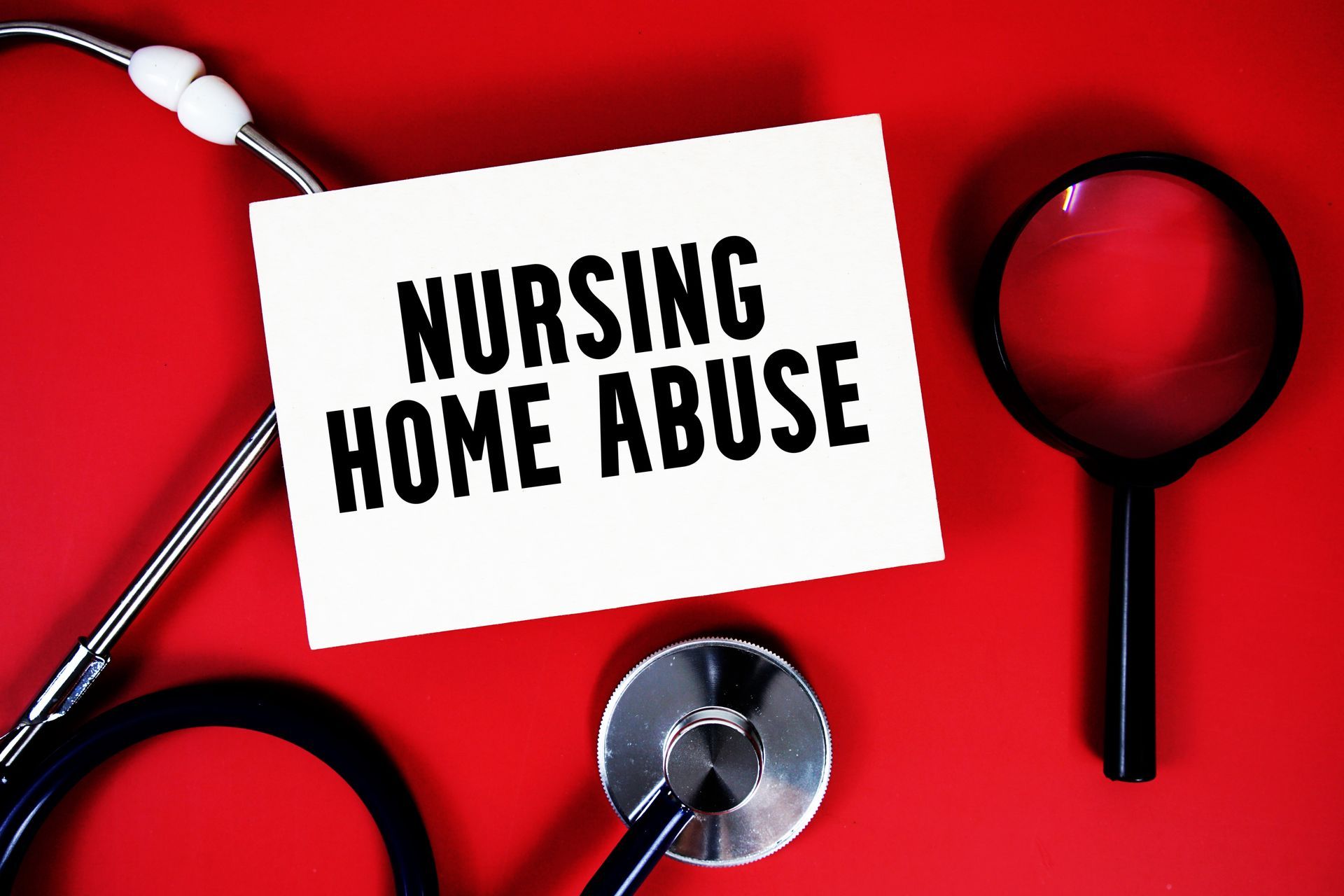 White card with NURSING HOME ABUSE on a red background, stethoscope, and magnifying glass.