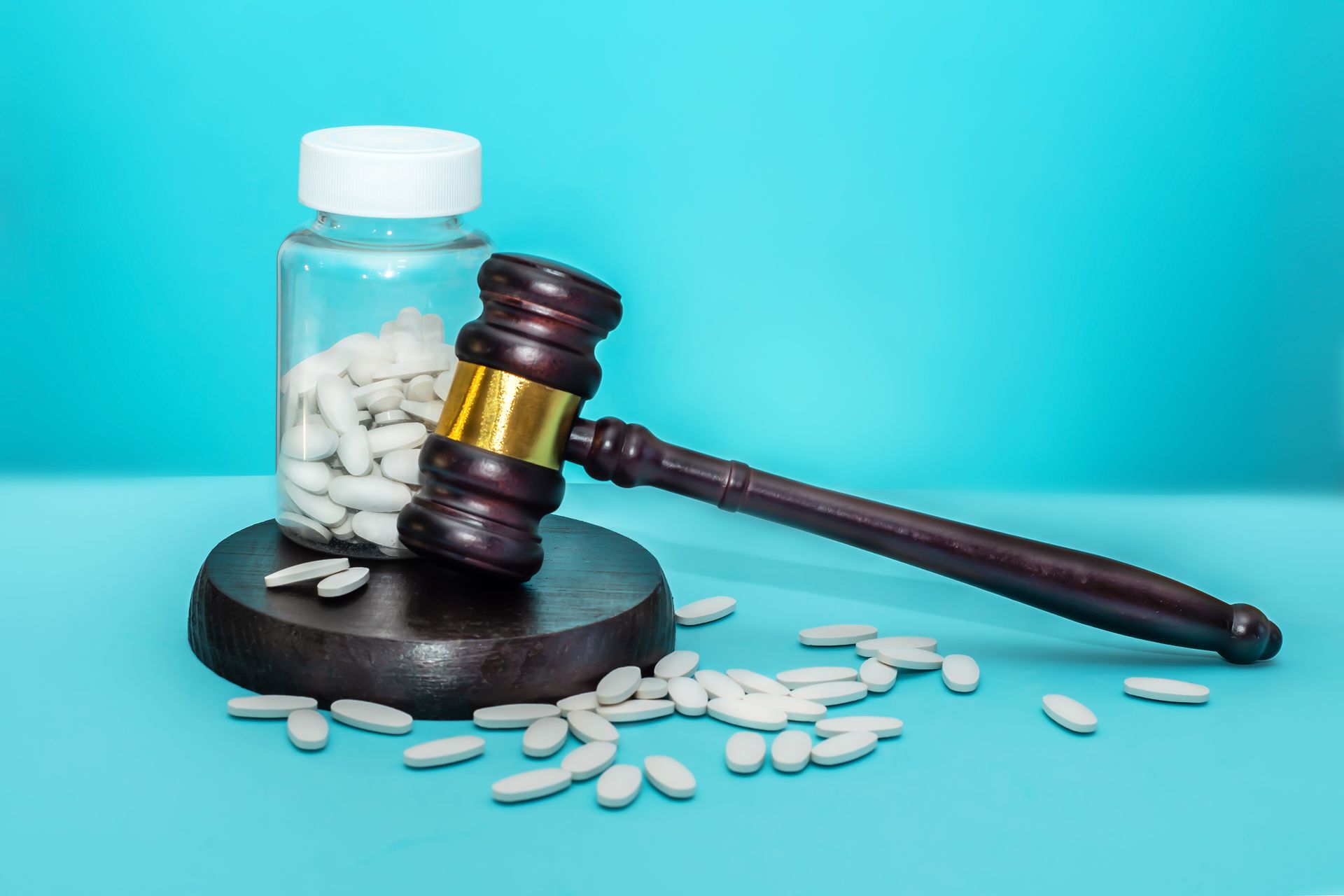 Brown gavel next to a clear pill bottle with white pills, scattered on a blue surface.
