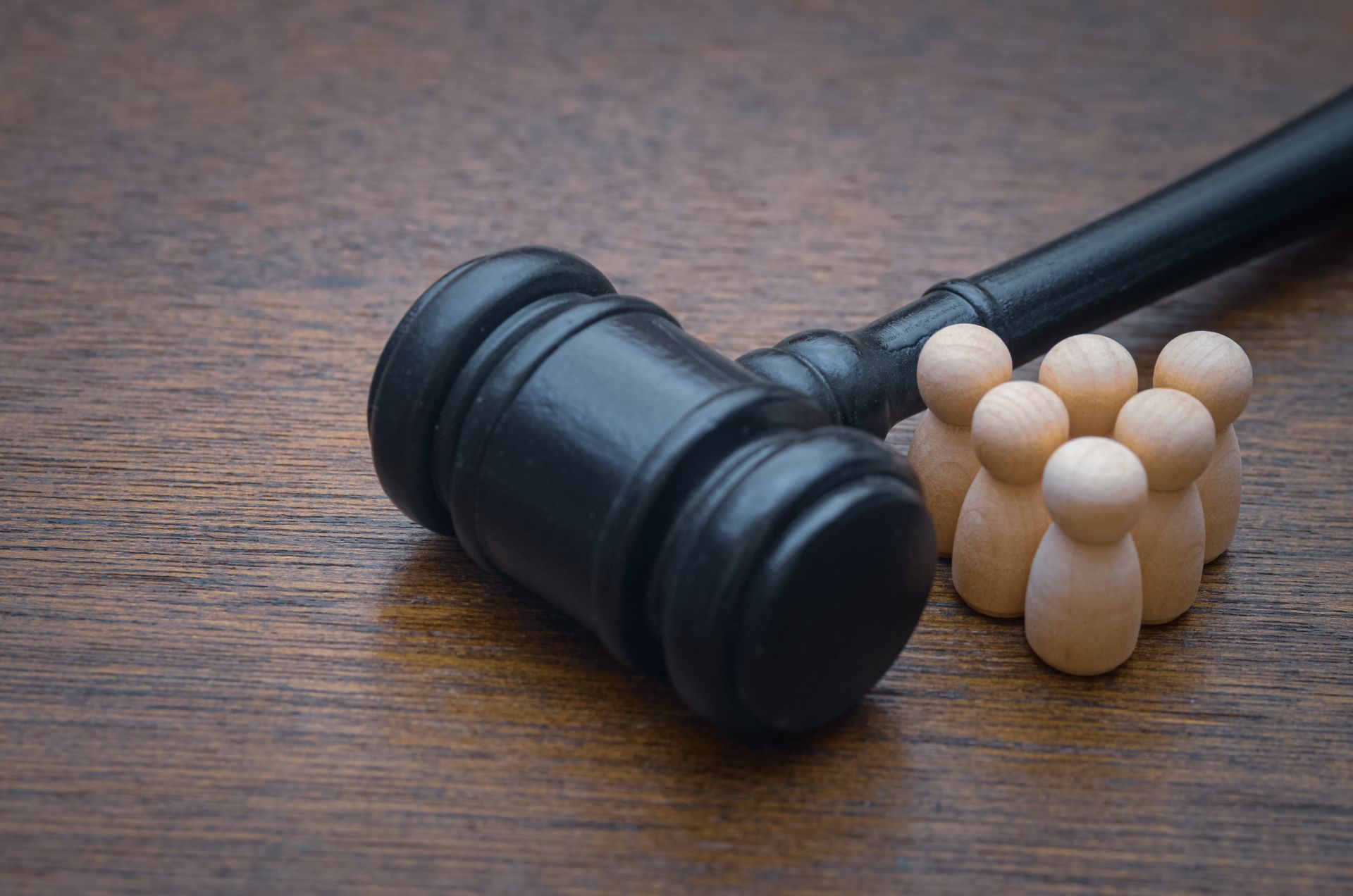 Wooden gavel next to a group of small wooden people figures on a wood surface.