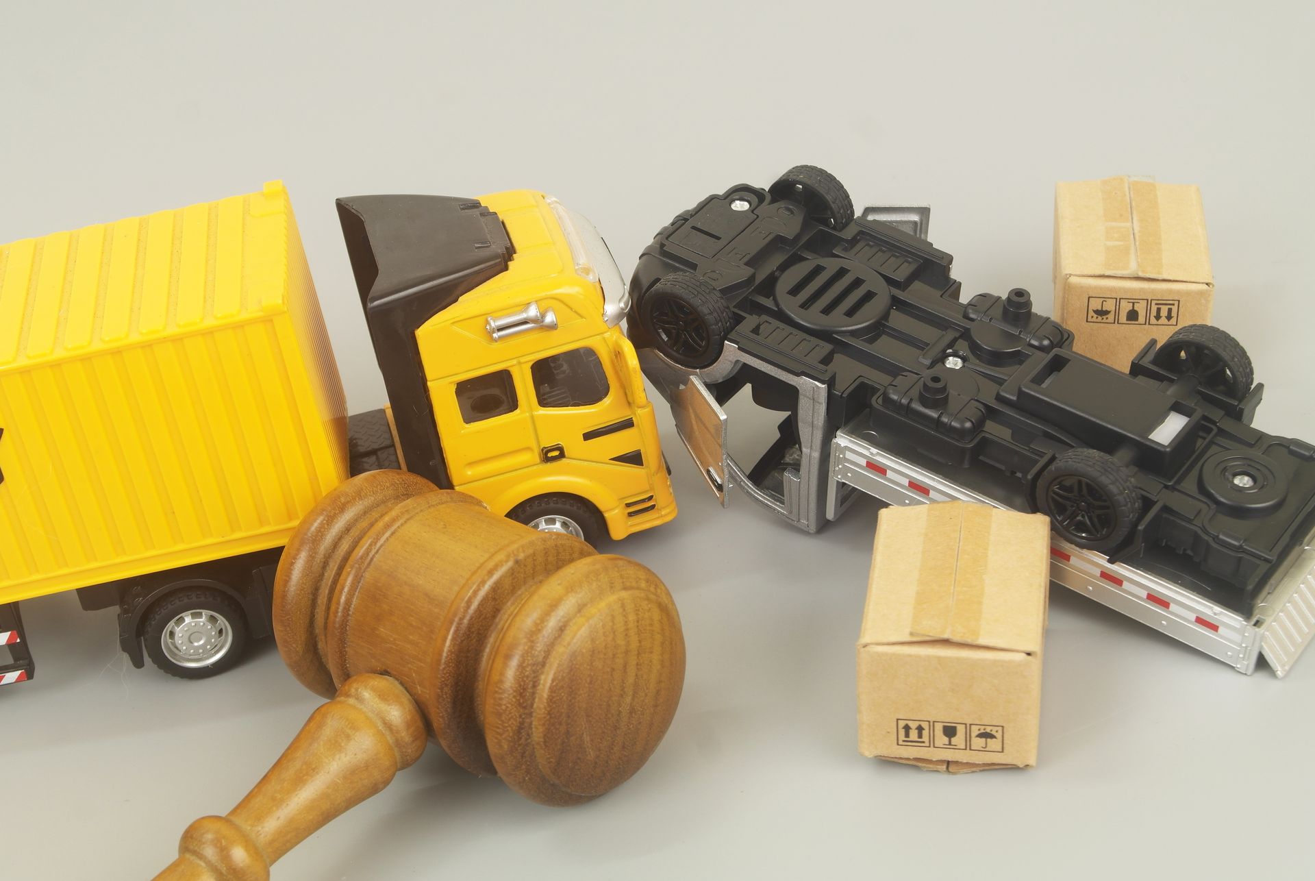Toy truck and overturned semi-truck with small boxes near a wooden gavel.