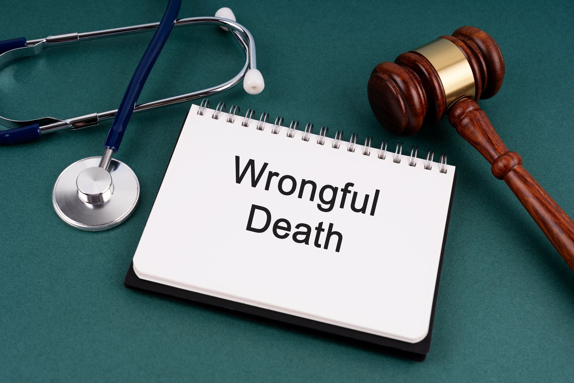 Notebook with Wrongful Death next to a gavel and stethoscope on a green surface.