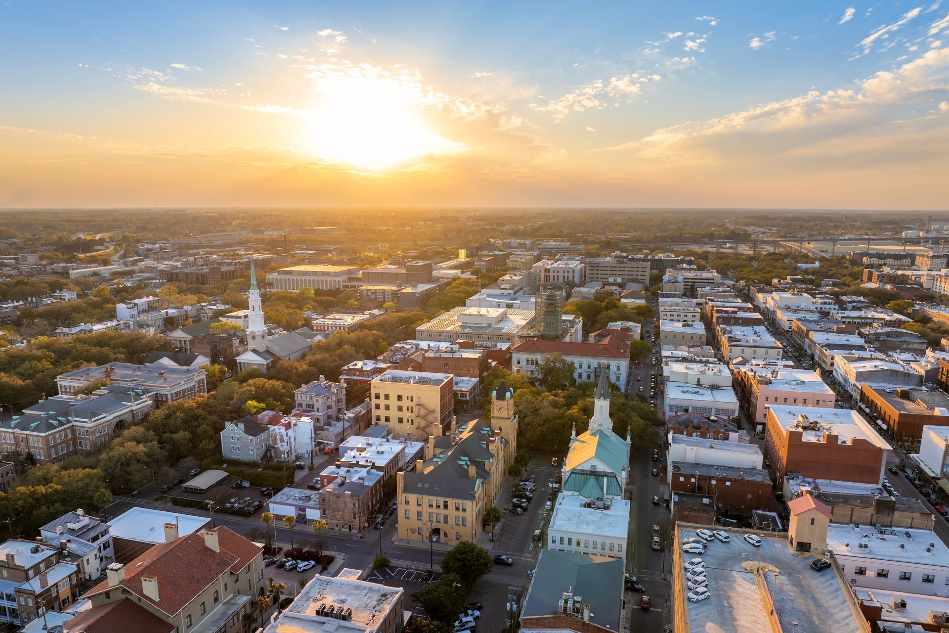 Aerial view of Savannah, Georgia at sunset with a cityscape of buildings and a church steeple.