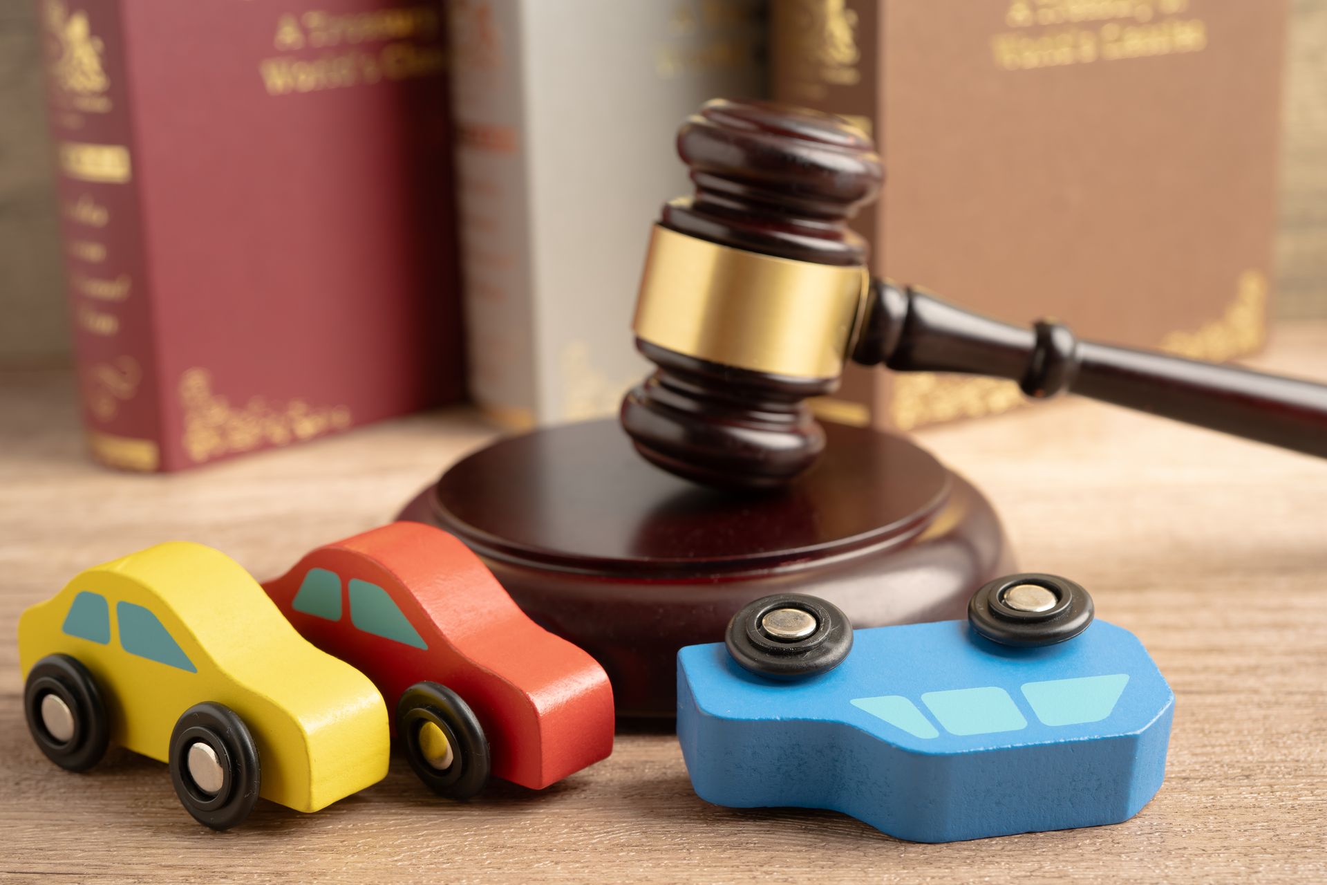 Toy cars and gavel on a wooden surface, with books in the background. One car is overturned.