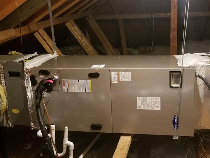 An air conditioner is hanging from the ceiling of an attic.