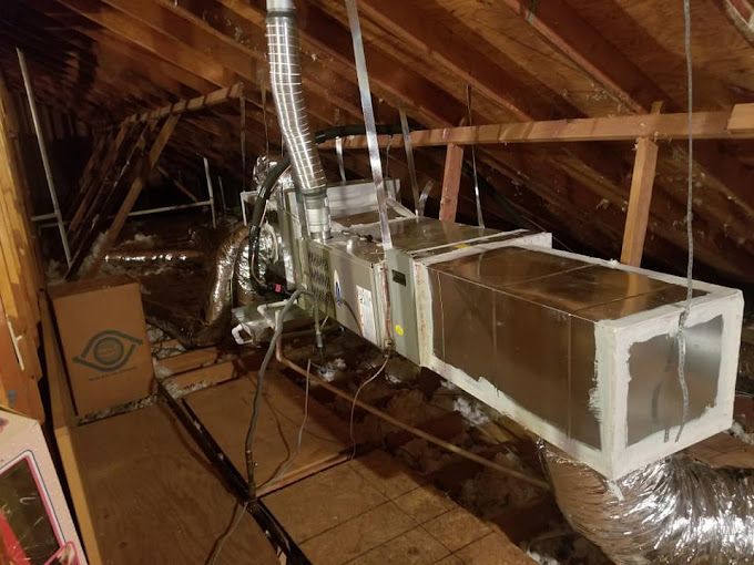 An air conditioner is hanging from the ceiling of an attic.