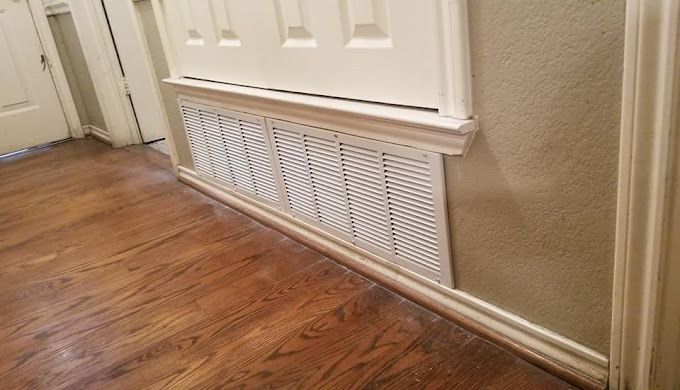 A hallway with hardwood floors and a white air vent on the wall.