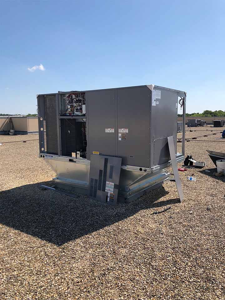 A large air conditioner is sitting on top of a gravel roof.