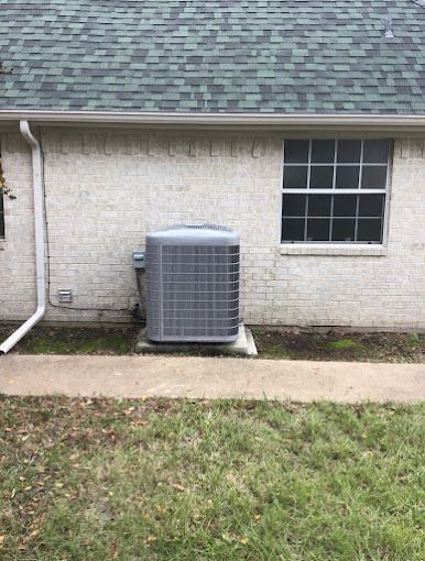 An air conditioner is sitting on the side of a brick house next to a window.
