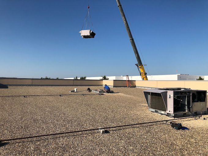 A crane is lifting a piece of equipment from the roof of a building.