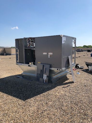 A large air conditioner is sitting on top of a gravel roof.
