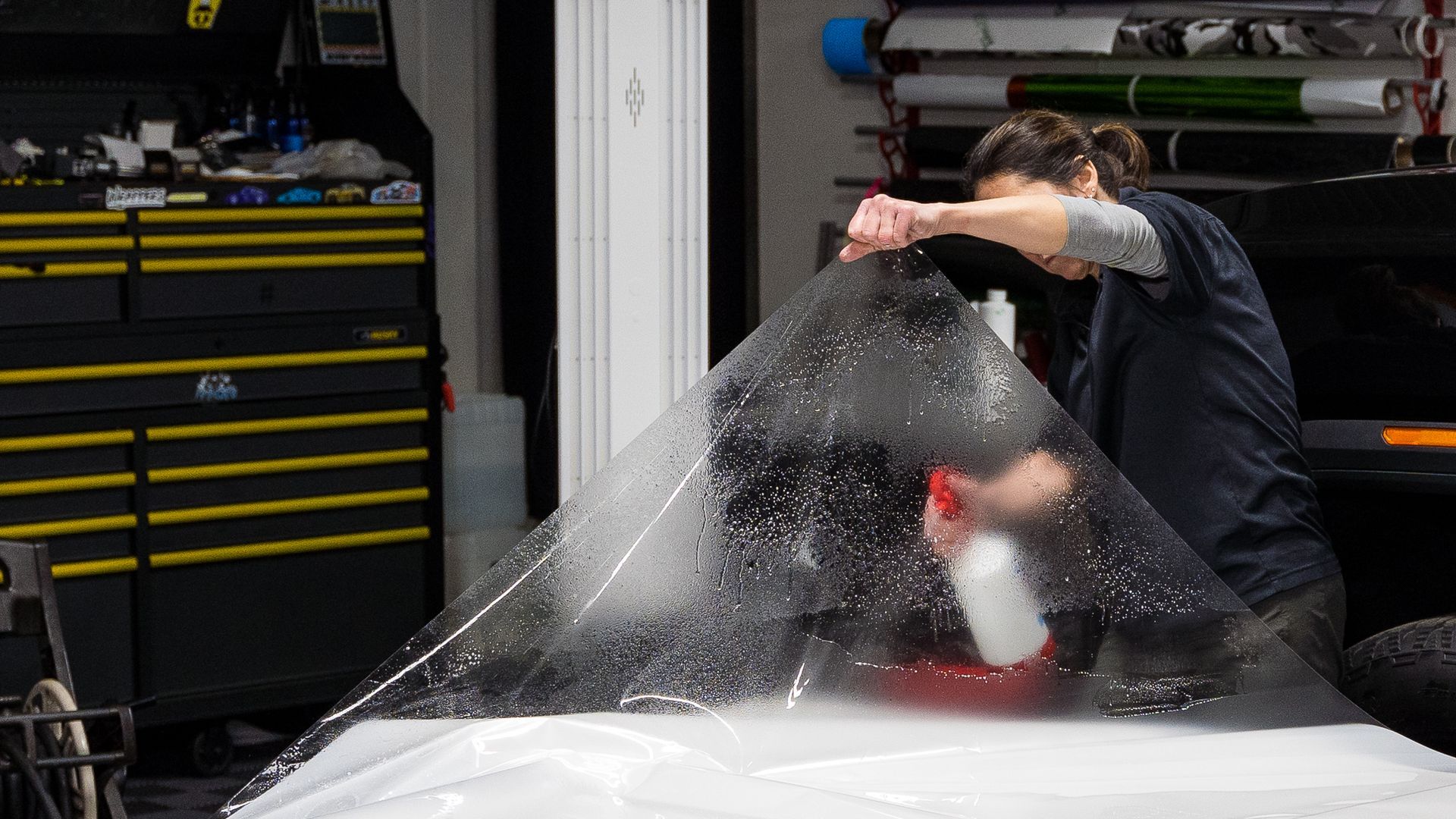 A woman is wrapping a car with plastic wrap in a garage.