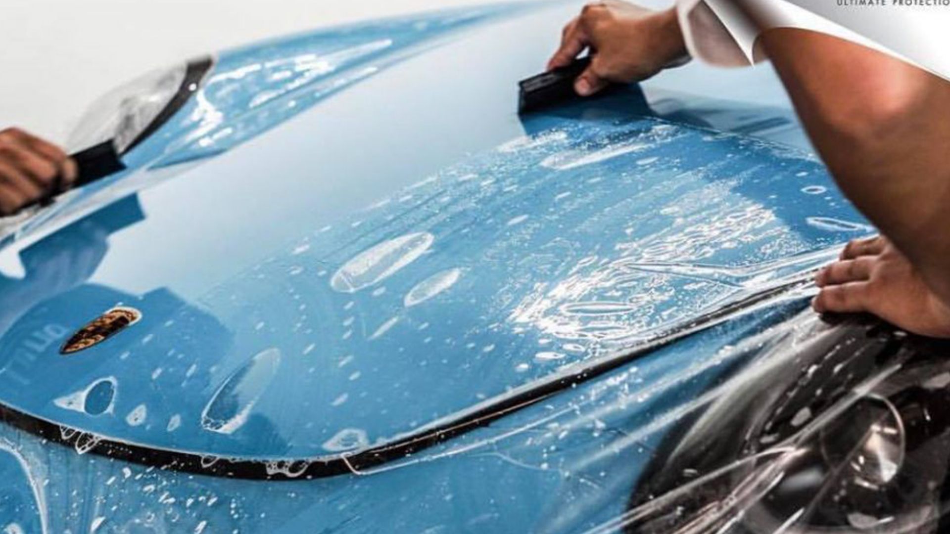 a person is applying a protective film to the hood of a car .