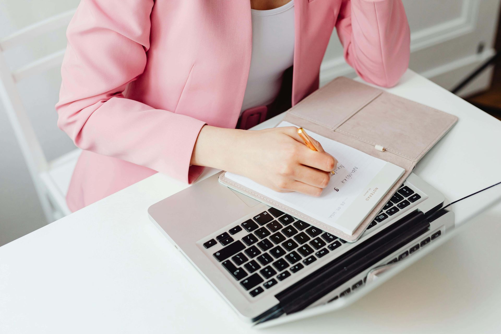 A woman is sitting at a desk with a laptop and a notebook.