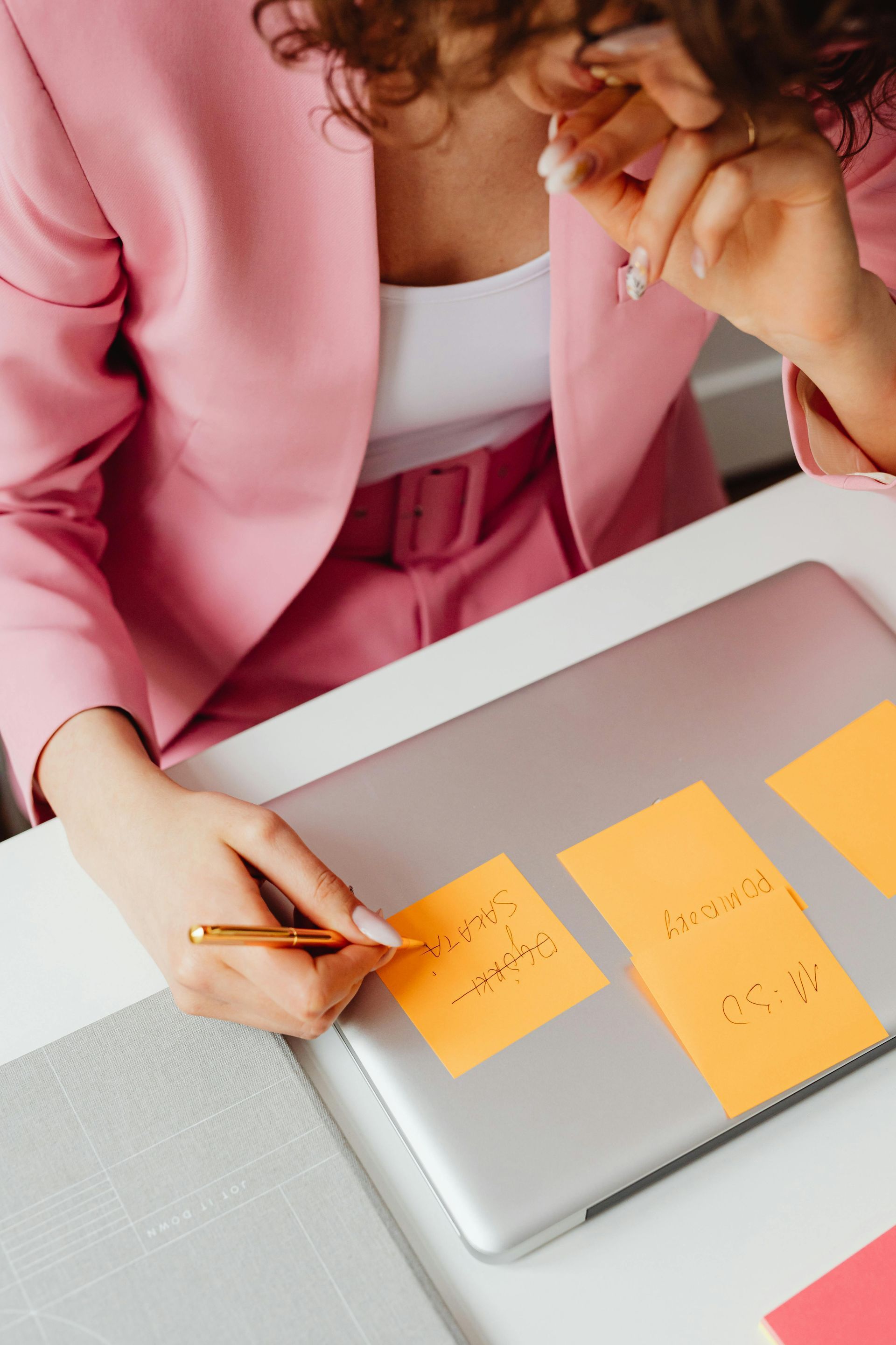 Woman in pink suit using a pen on sticky notes attached to a laptop.