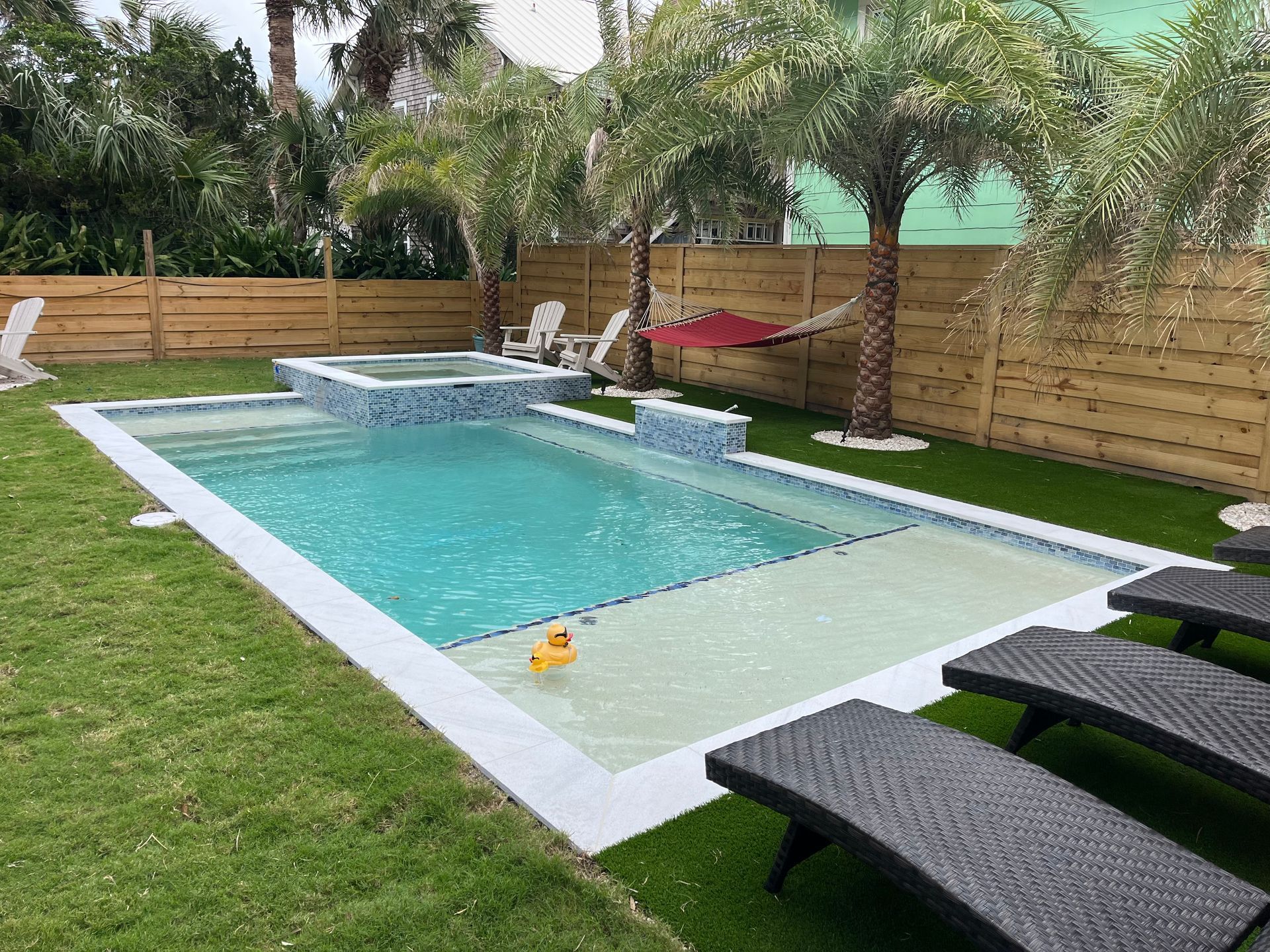 A large swimming pool surrounded by chairs and palm trees in a backyard.