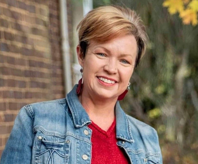 A woman wearing a denim jacket and a red sweater is smiling for the camera.