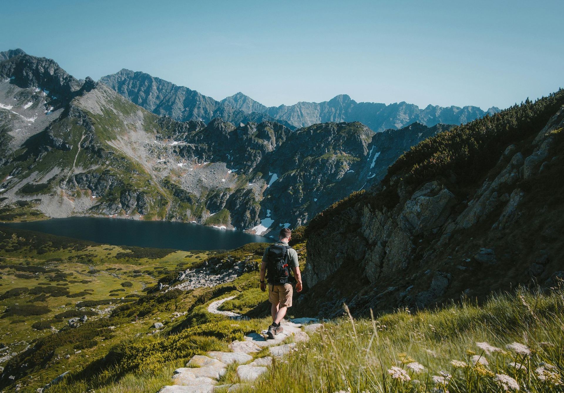 A man with a backpack is walking down a path in the mountains.