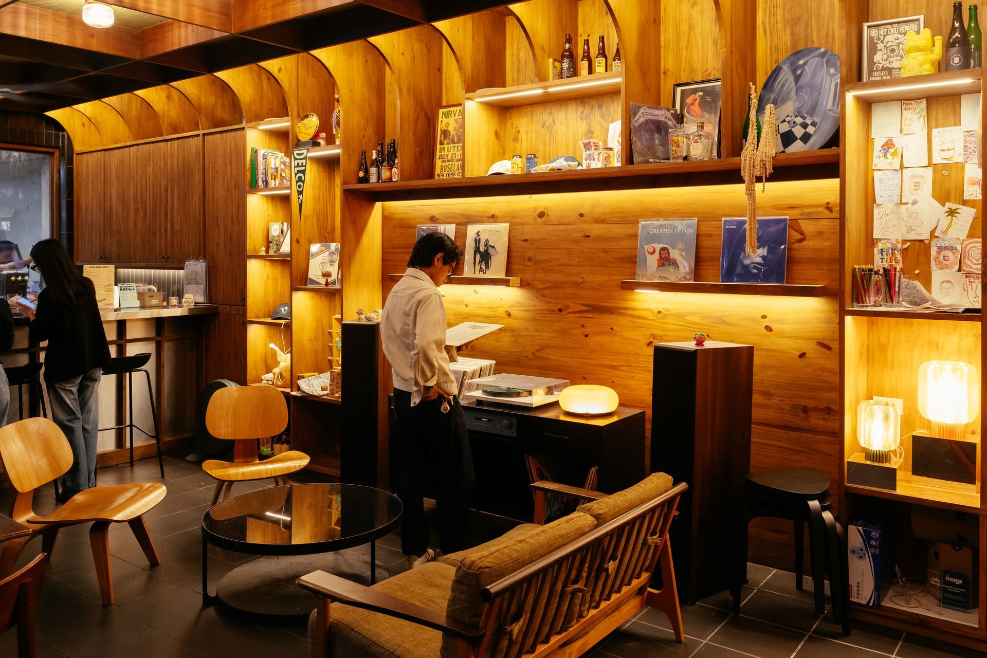 A cozy room with wood paneling. A person near a record player. Shelves with records and lamps.