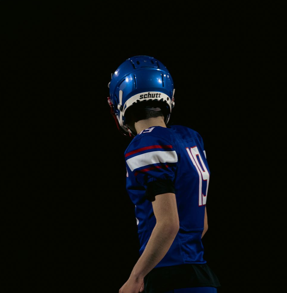 A football player in a blue uniform with the number 9, seen from behind against a black background.