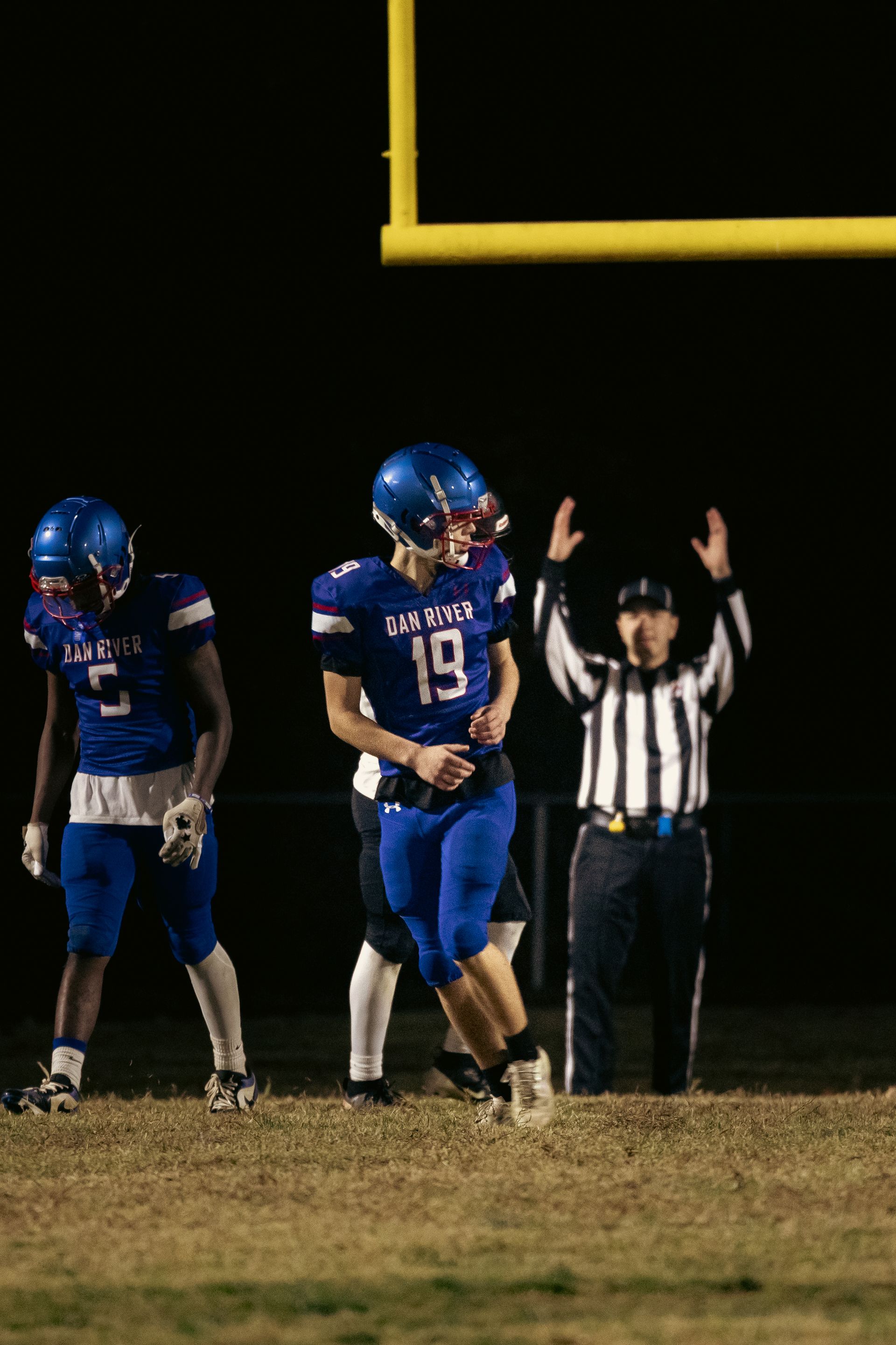 Football players in blue uniforms on a field at night, while a referee signals a successful goal near the goalposts.