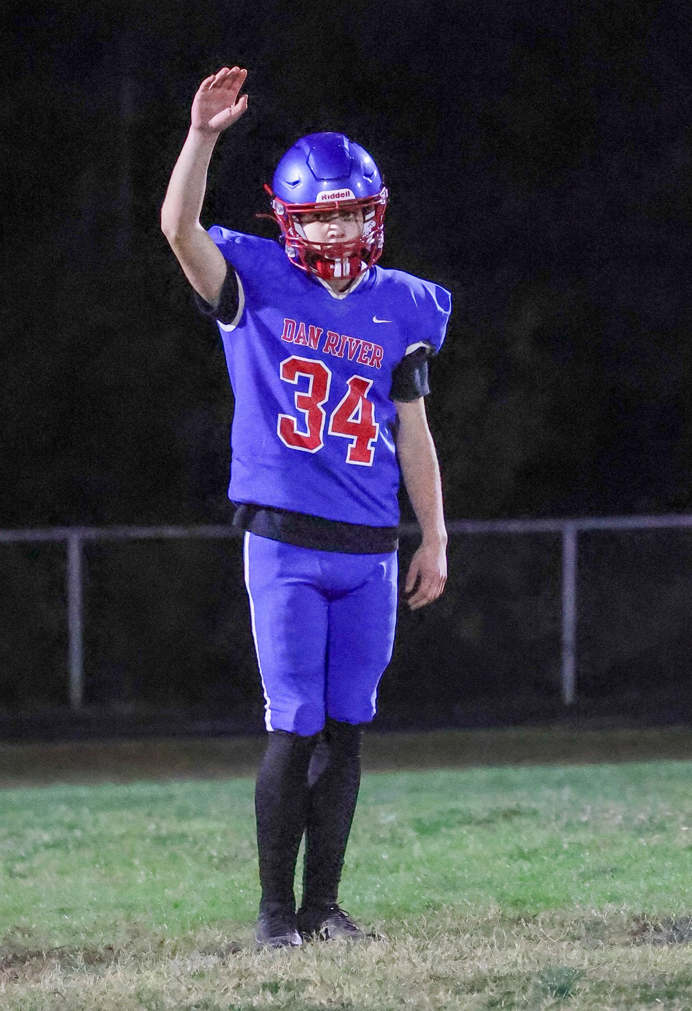 A football player wearing a blue uniform with the number 34 and a blue helmet raises one hand while standing on a field.