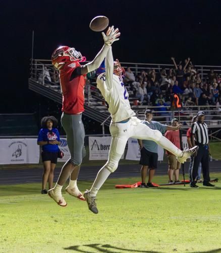 Two football players in red and white uniforms leap toward a ball in mid-air during a nighttime game.
