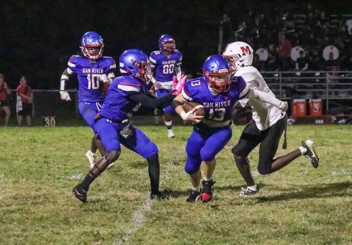 A football player in a blue uniform runs with the ball while being pursued by a player in a white uniform on a field.