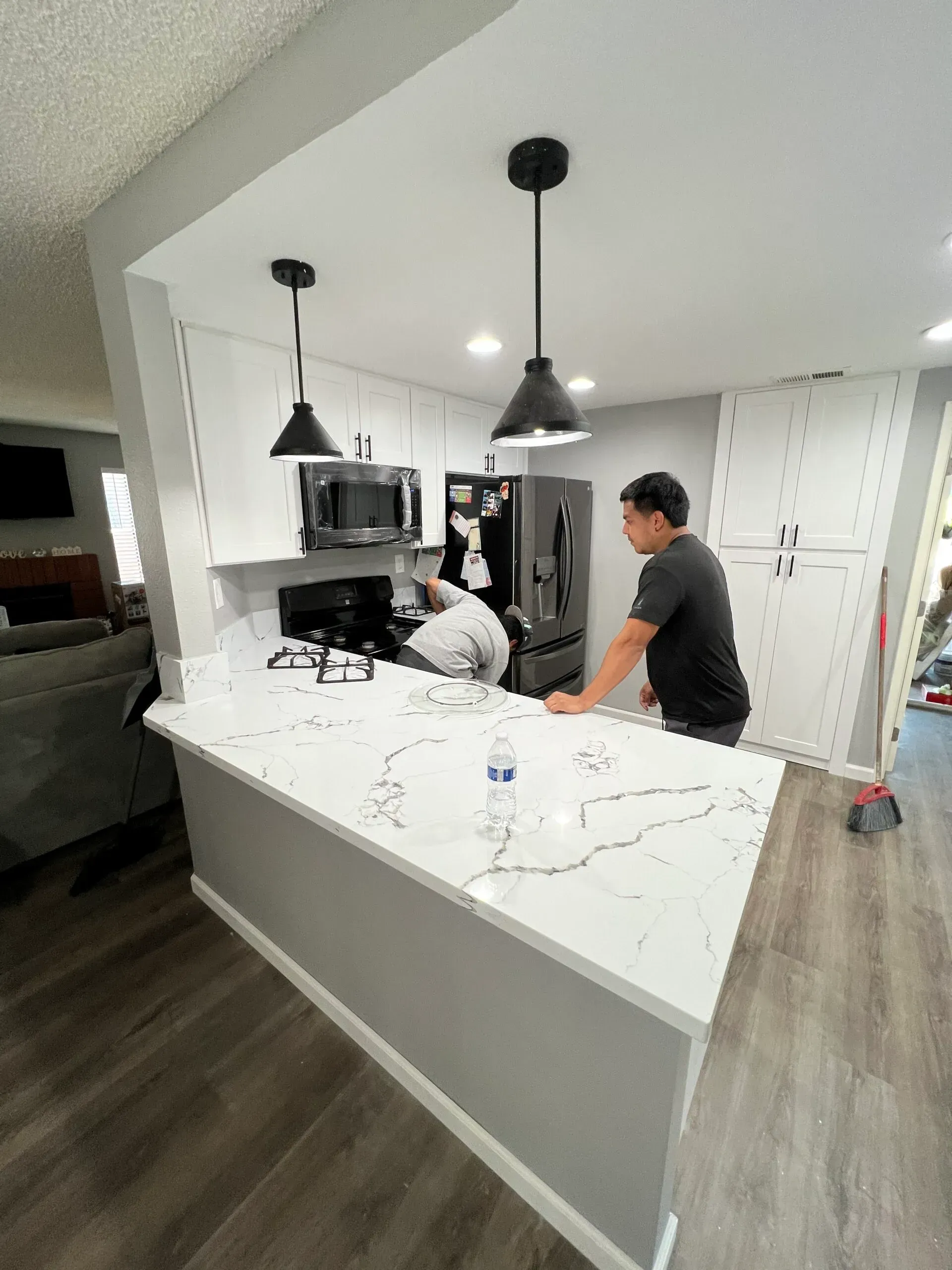 Kitchen remodel: Workers near a peninsula with white countertops, black pendant lights.