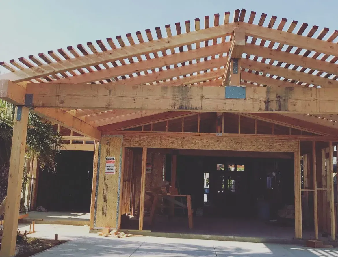Wooden frame of a garage under construction with an overhead trellis. Bright sunny day.