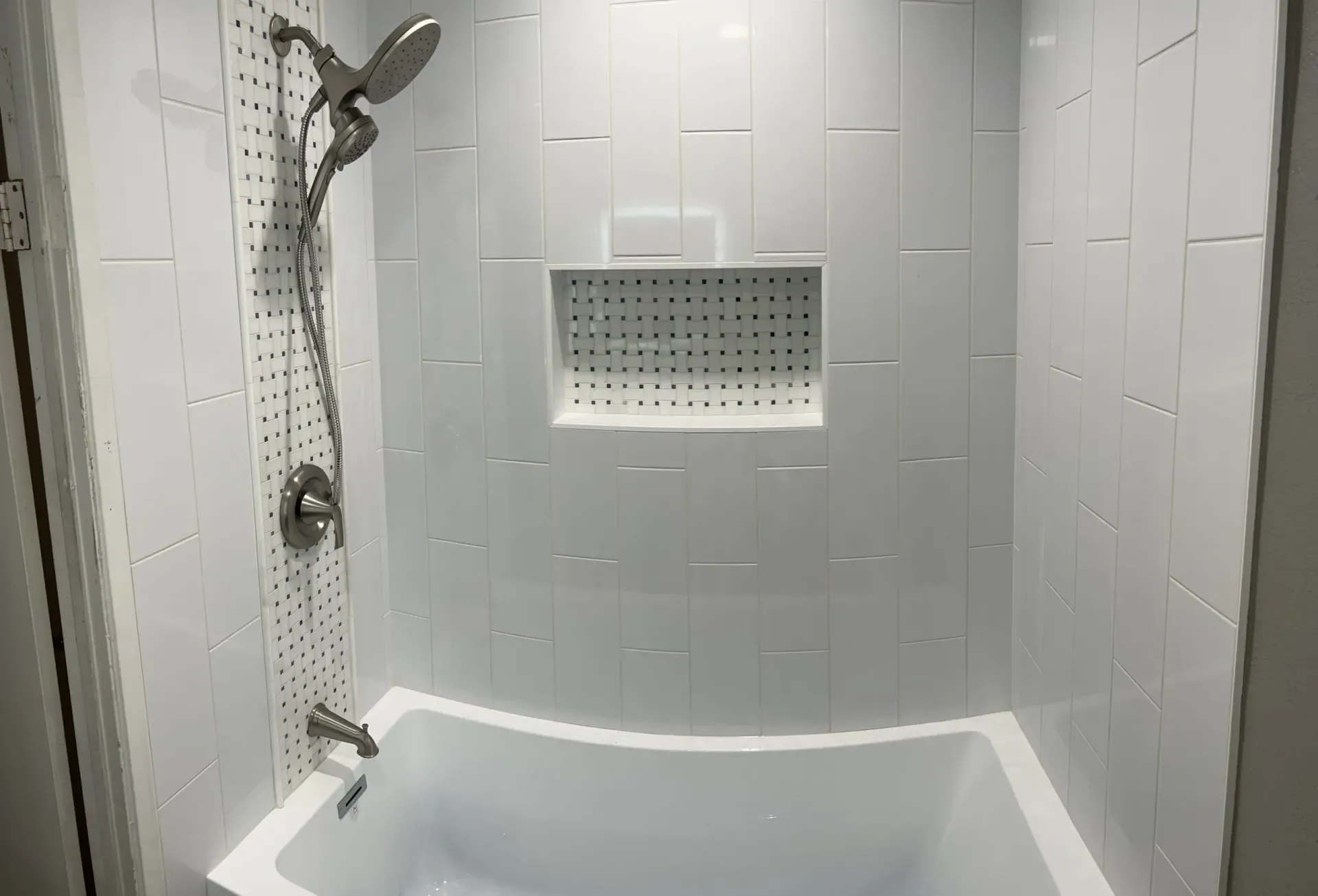 White bathroom with a tub, shower head, and tiled walls.