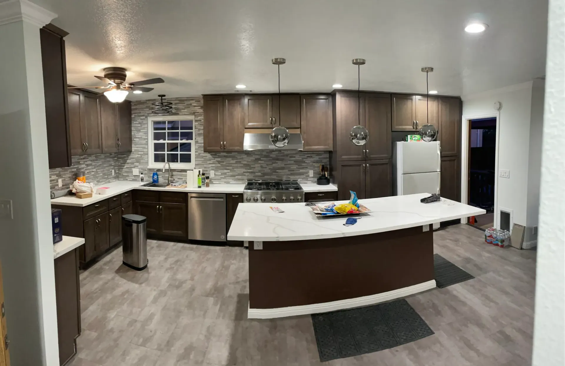 Spacious kitchen with dark brown cabinets, white countertops, and a large island. Gray flooring.