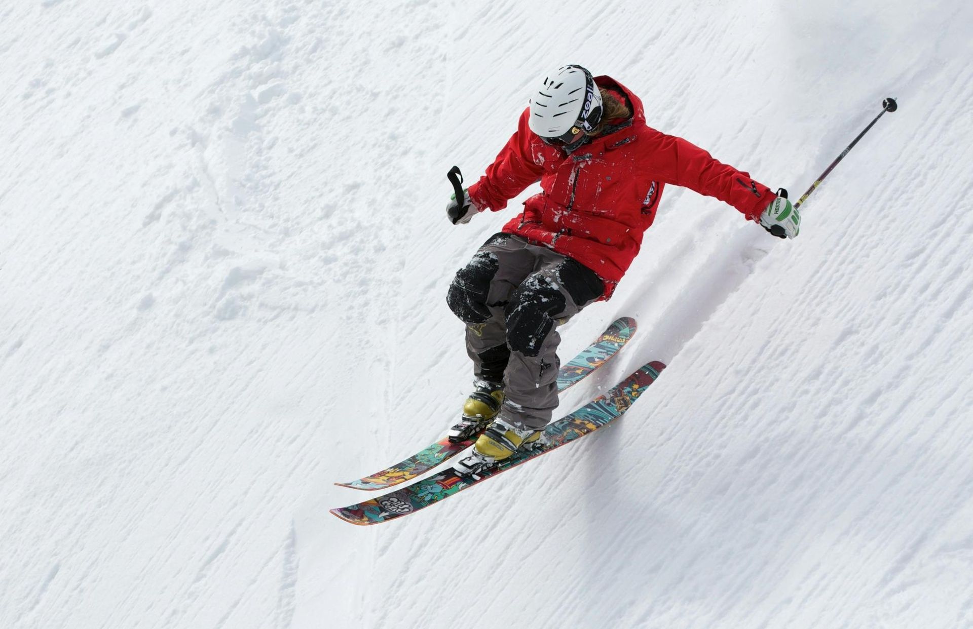 Skier in red jacket carves down a snow-covered slope, with white helmet and poles.