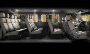 Interior of a van with multiple rows of gray seats. The driver's seat and dashboard are visible on the right.