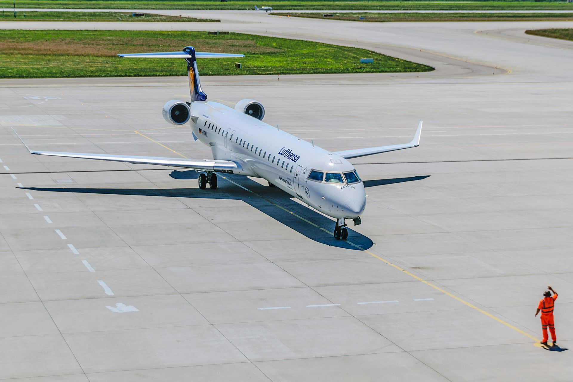 A white airplane on the tarmac with a person in an orange suit directing it.