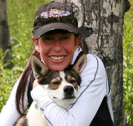 Woman hugs a dog. They are smiling. Outdoors, near a tree.