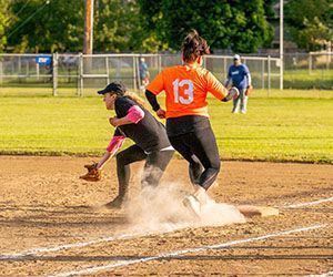 Two softball players collide at base, kicking up dust during a game.