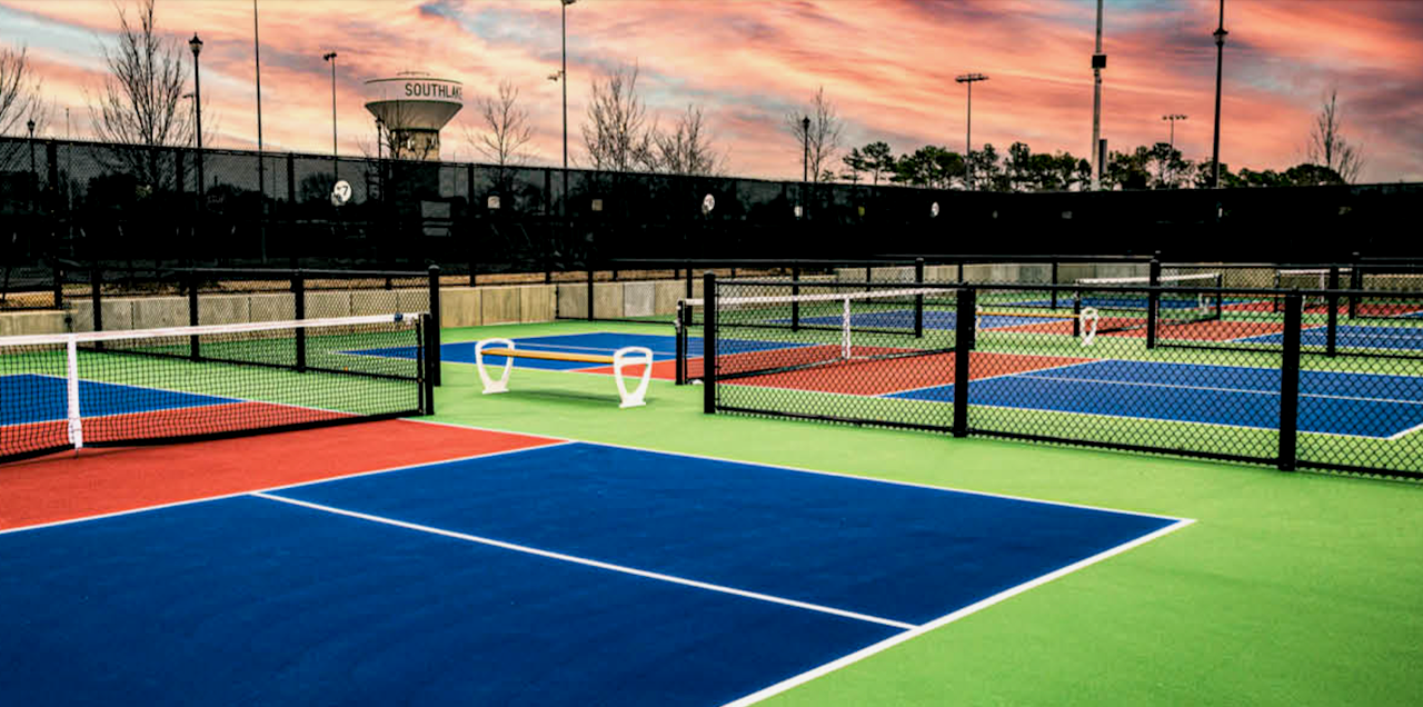 A tennis court with a fence around it and a sunset in the background.
