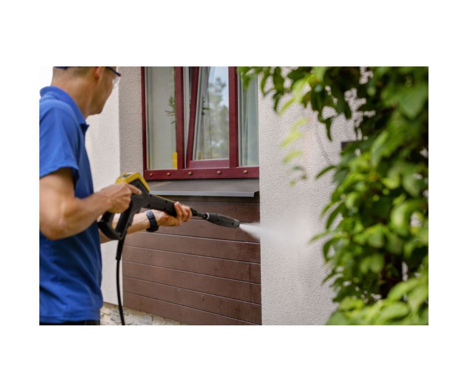 picture of man in blue shirt using pressure washer on side of house