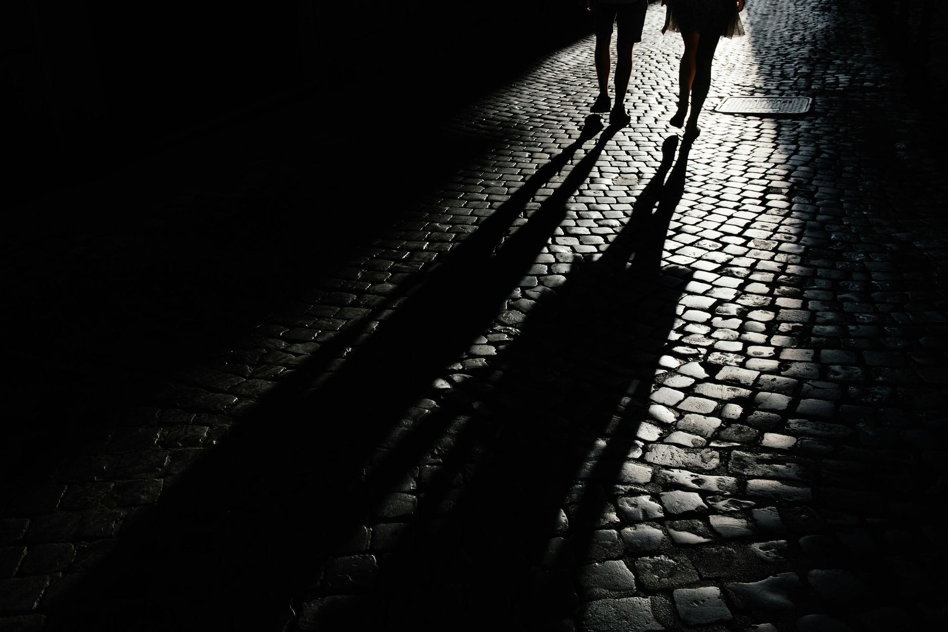 Two people are walking down a cobblestone street at night.
